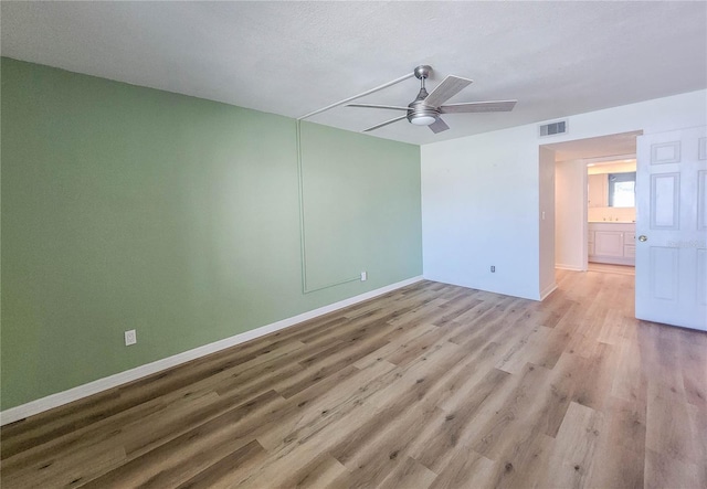 spare room with baseboards, light wood-type flooring, visible vents, and a ceiling fan