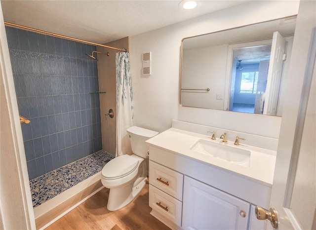 bathroom featuring toilet, wood finished floors, visible vents, vanity, and a tile shower