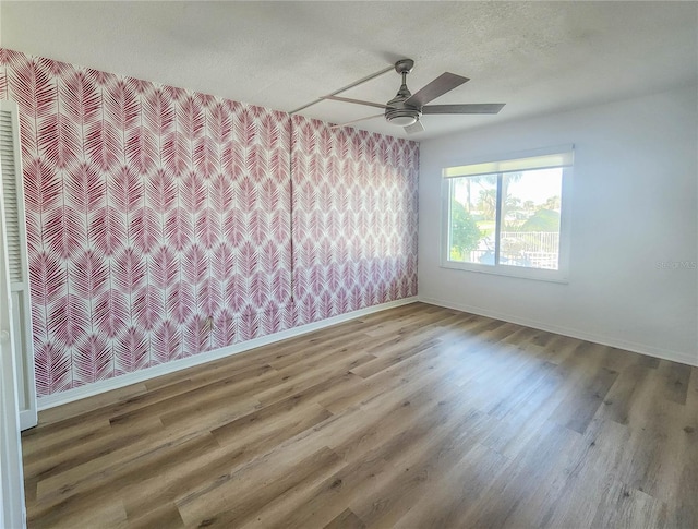 unfurnished room featuring ceiling fan, a textured ceiling, wood finished floors, baseboards, and wallpapered walls