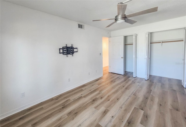 unfurnished bedroom with wood finished floors, a ceiling fan, visible vents, baseboards, and two closets