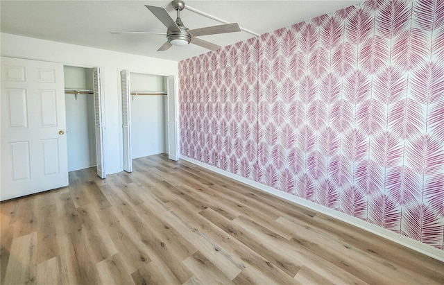 unfurnished bedroom featuring light wood finished floors, two closets, ceiling fan, baseboards, and wallpapered walls