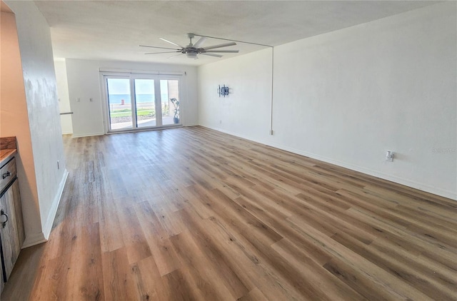 unfurnished living room featuring a ceiling fan, baseboards, and wood finished floors