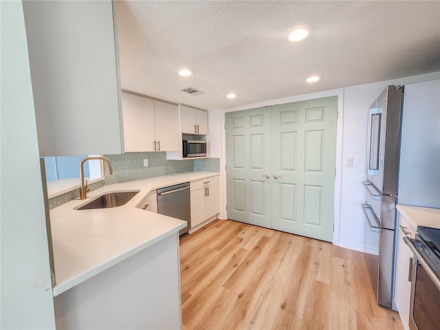 kitchen featuring visible vents, white cabinets, stainless steel appliances, light wood-style floors, and a sink