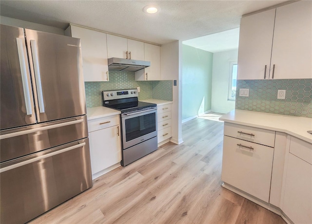 kitchen with under cabinet range hood, stainless steel appliances, white cabinets, light countertops, and light wood finished floors