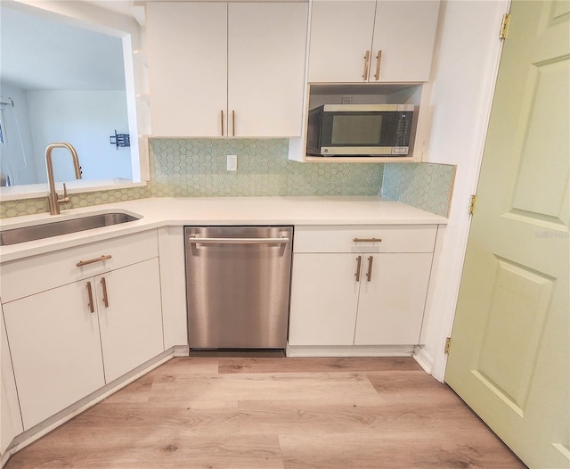 kitchen with stainless steel appliances, a sink, white cabinets, light countertops, and light wood-type flooring