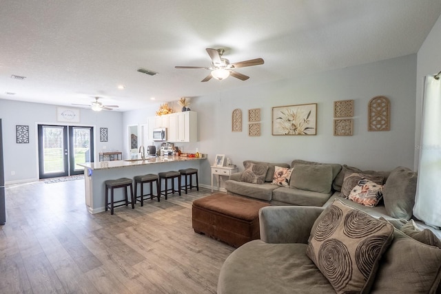 living room featuring light wood finished floors, visible vents, a ceiling fan, a textured ceiling, and baseboards