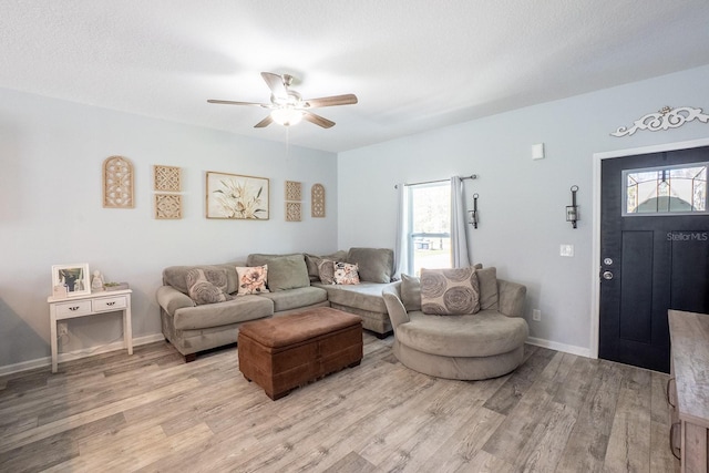 living area with light wood-style flooring, a textured ceiling, baseboards, and a ceiling fan