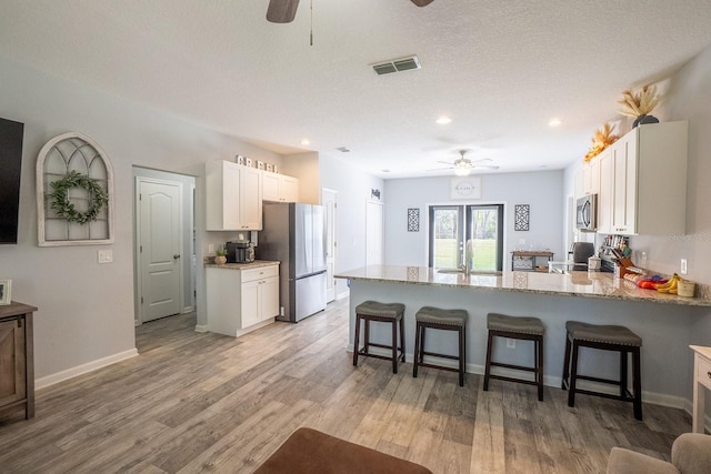 kitchen featuring stainless steel appliances, a breakfast bar area, visible vents, and white cabinets