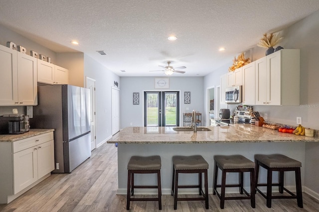 kitchen with a textured ceiling, stainless steel appliances, a peninsula, a sink, and light wood-type flooring