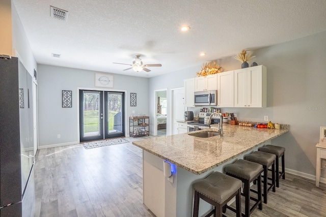 kitchen featuring a breakfast bar area, visible vents, light wood-style floors, white cabinetry, and appliances with stainless steel finishes