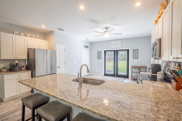 kitchen with stainless steel appliances, a sink, french doors, light wood-type flooring, and light stone countertops