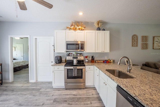 kitchen with light stone counters, light wood-style flooring, stainless steel appliances, a sink, and white cabinetry