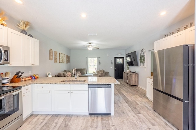 kitchen with a peninsula, white cabinets, stainless steel appliances, and a sink