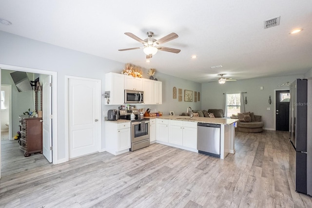 kitchen with appliances with stainless steel finishes, open floor plan, white cabinetry, a sink, and a peninsula