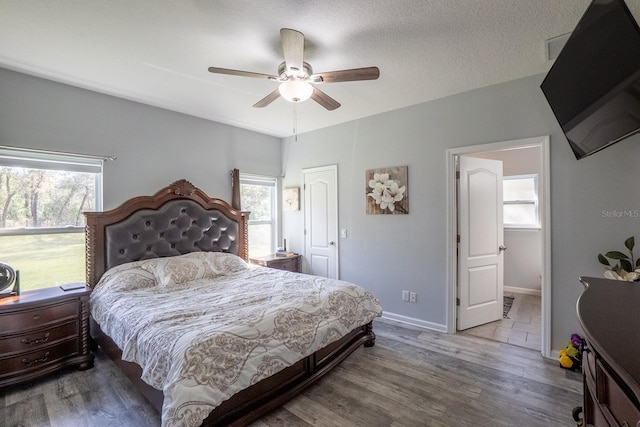 bedroom with a textured ceiling, multiple windows, wood finished floors, and baseboards