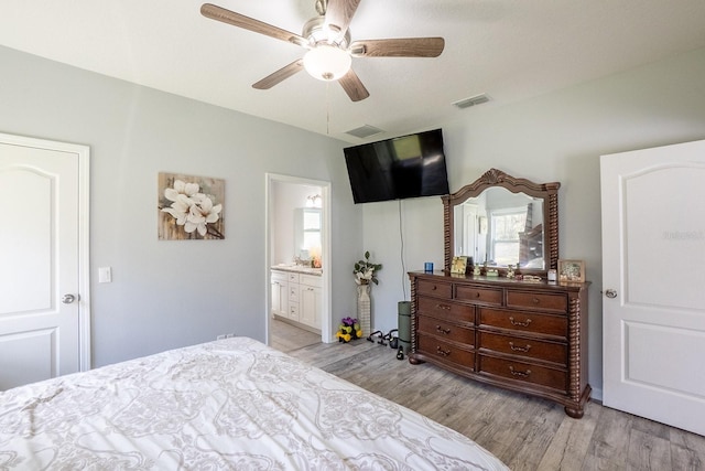 bedroom featuring light wood-style floors, visible vents, ensuite bathroom, and a ceiling fan