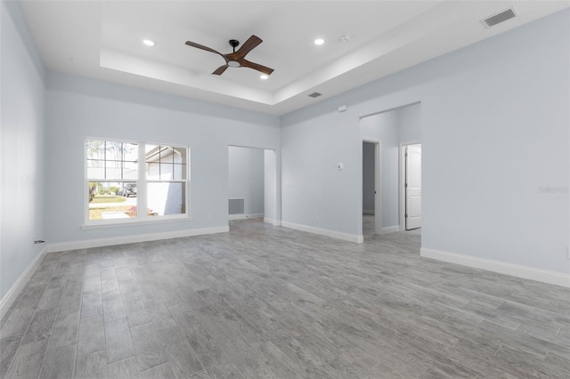 interior space featuring light wood-style floors, baseboards, visible vents, and a raised ceiling