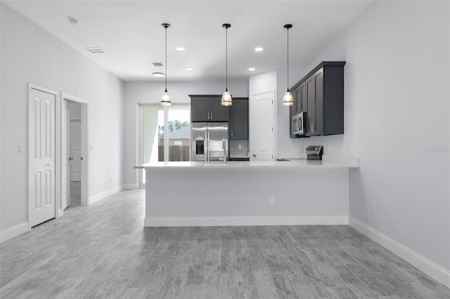 kitchen featuring stainless steel appliances, a peninsula, hanging light fixtures, light countertops, and light wood-type flooring