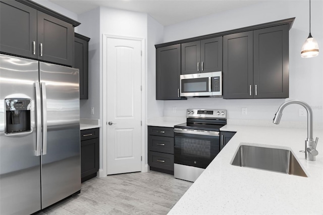 kitchen featuring pendant lighting, stainless steel appliances, light wood-style floors, a sink, and light stone countertops