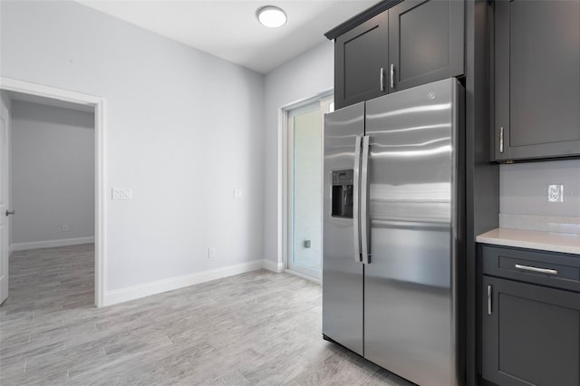 kitchen featuring light wood-style floors, stainless steel fridge, baseboards, and light countertops