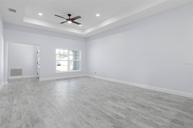 unfurnished room featuring a tray ceiling, light wood-type flooring, visible vents, and baseboards