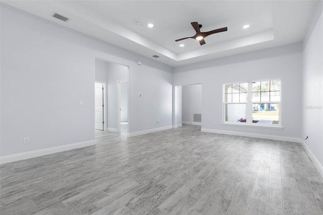 empty room featuring recessed lighting, a raised ceiling, visible vents, light wood-style floors, and baseboards