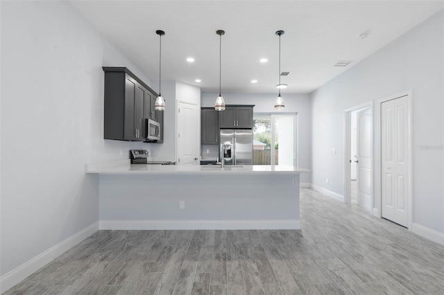 kitchen featuring light countertops, light wood-style flooring, appliances with stainless steel finishes, a peninsula, and baseboards