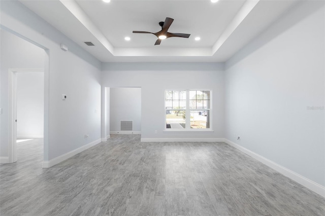 empty room with light wood finished floors, recessed lighting, a raised ceiling, visible vents, and baseboards