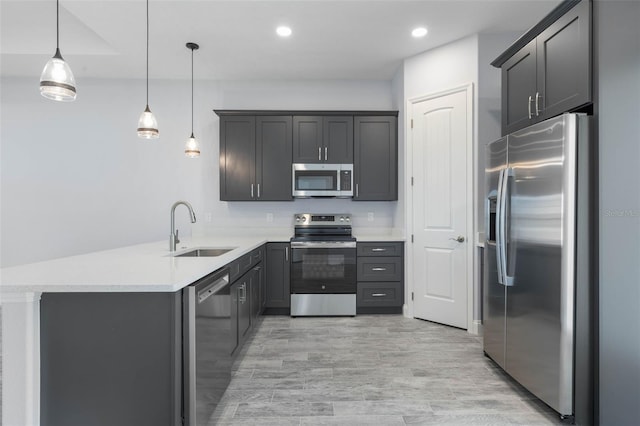 kitchen featuring light countertops, hanging light fixtures, appliances with stainless steel finishes, a sink, and a peninsula