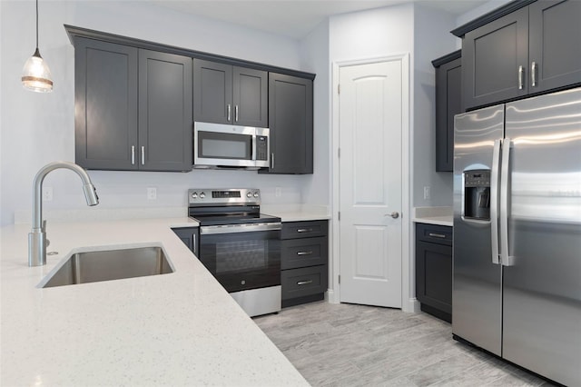 kitchen featuring light wood-style flooring, stainless steel appliances, a sink, light stone countertops, and decorative light fixtures