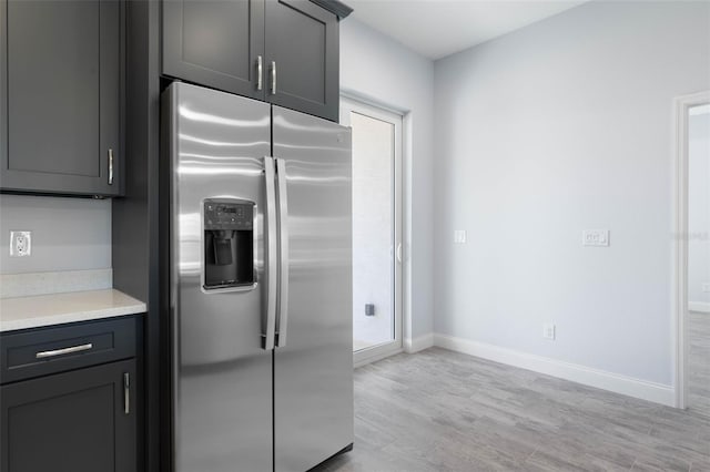 kitchen with light wood-style flooring, light countertops, stainless steel refrigerator with ice dispenser, and baseboards