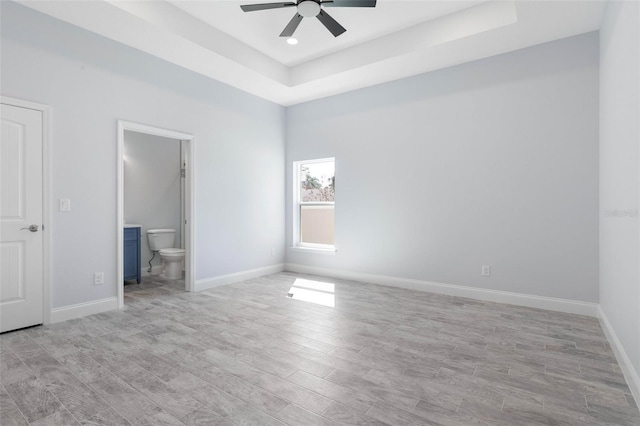 unfurnished bedroom featuring light wood-style floors, a raised ceiling, baseboards, and ensuite bathroom