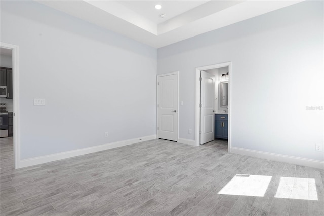 unfurnished bedroom with recessed lighting, ensuite bath, baseboards, light wood-type flooring, and a raised ceiling