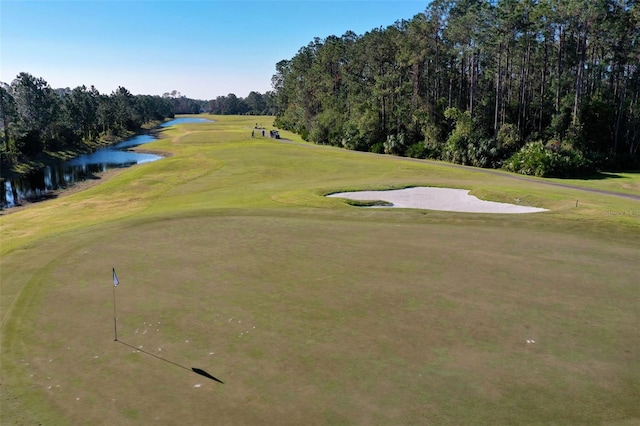 view of home's community featuring view of golf course, a water view, a yard, and a wooded view