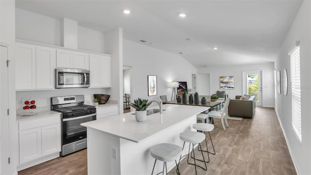 kitchen featuring an island with sink, appliances with stainless steel finishes, open floor plan, vaulted ceiling, and white cabinetry