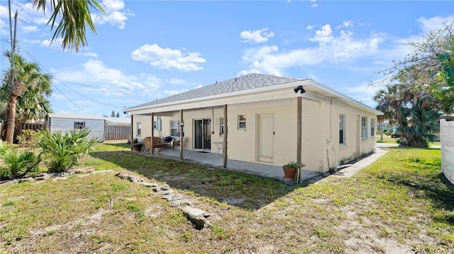 back of house with an outbuilding, roof with shingles, a lawn, a patio area, and fence