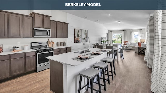 kitchen featuring a breakfast bar, a center island with sink, stainless steel appliances, a sink, and light wood-type flooring