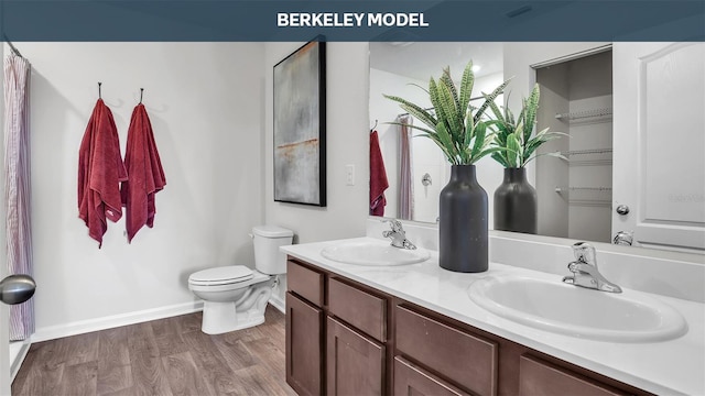 full bath featuring double vanity, a sink, toilet, and wood finished floors