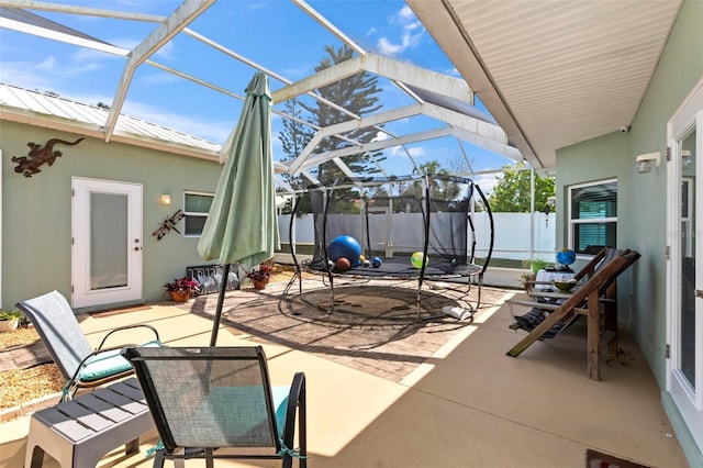 view of patio / terrace featuring glass enclosure, a trampoline, and fence