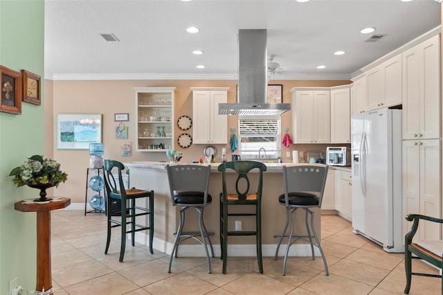 kitchen featuring island exhaust hood, white refrigerator with ice dispenser, crown molding, and a kitchen breakfast bar