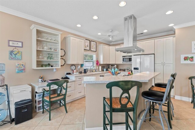 kitchen featuring island range hood, ornamental molding, white refrigerator with ice dispenser, a kitchen breakfast bar, and a center island