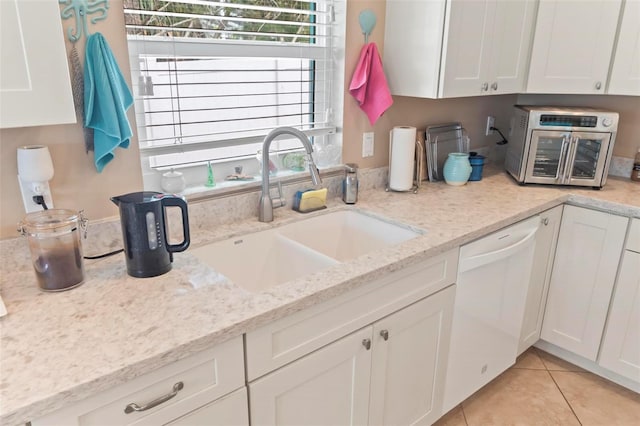 kitchen featuring light tile patterned floors, light stone countertops, a sink, white cabinets, and dishwasher