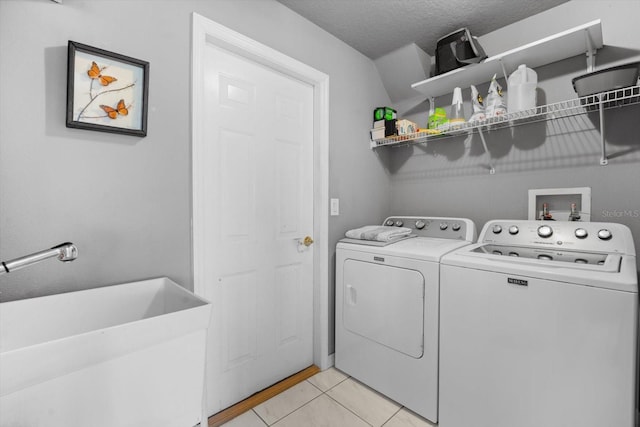 clothes washing area with light tile patterned floors, a sink, a textured ceiling, washer and dryer, and laundry area