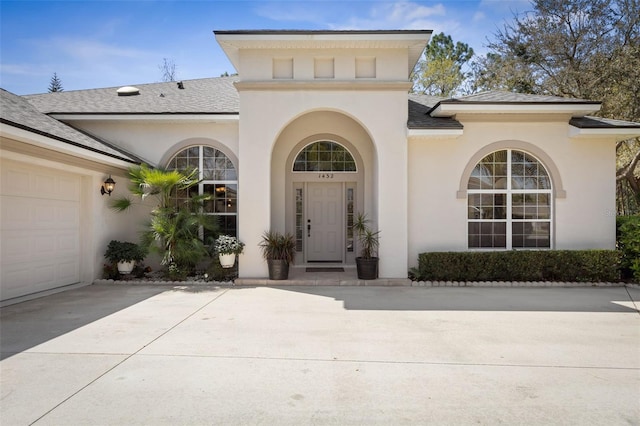 view of exterior entry featuring stucco siding, driveway, an attached garage, and a shingled roof