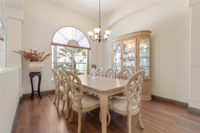 dining area with light wood finished floors, a chandelier, baseboards, and vaulted ceiling