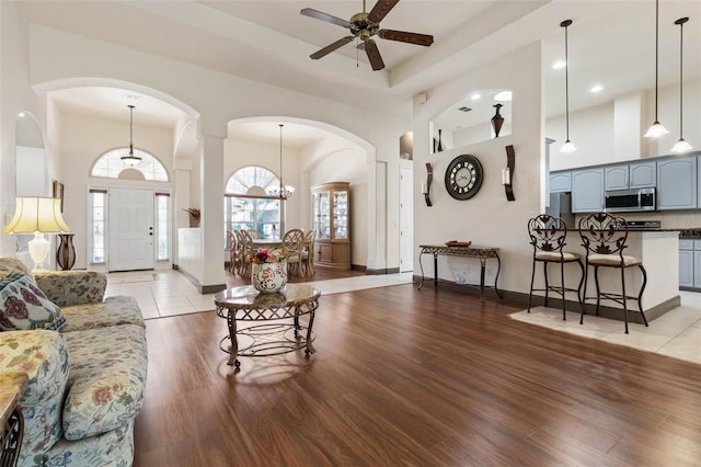 living area featuring light wood-style flooring, a towering ceiling, and ceiling fan with notable chandelier