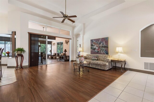 living room with visible vents, a ceiling fan, wood finished floors, baseboards, and a towering ceiling