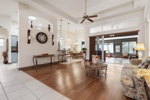 living room with a ceiling fan, wood finished floors, arched walkways, baseboards, and a towering ceiling