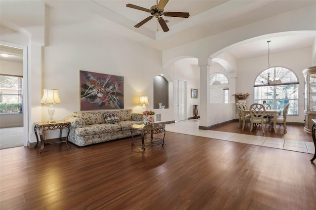 living area featuring a healthy amount of sunlight, ceiling fan with notable chandelier, a towering ceiling, and wood finished floors