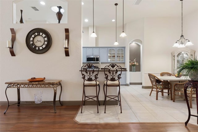 kitchen featuring arched walkways, stainless steel microwave, light wood-style floors, and visible vents